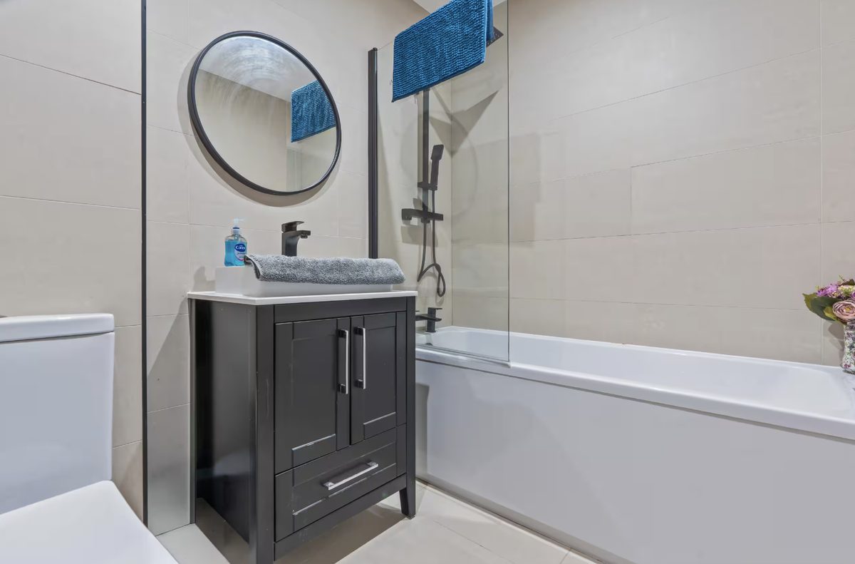 Bathroom with a dark grey vanity, round mirror and bathtub